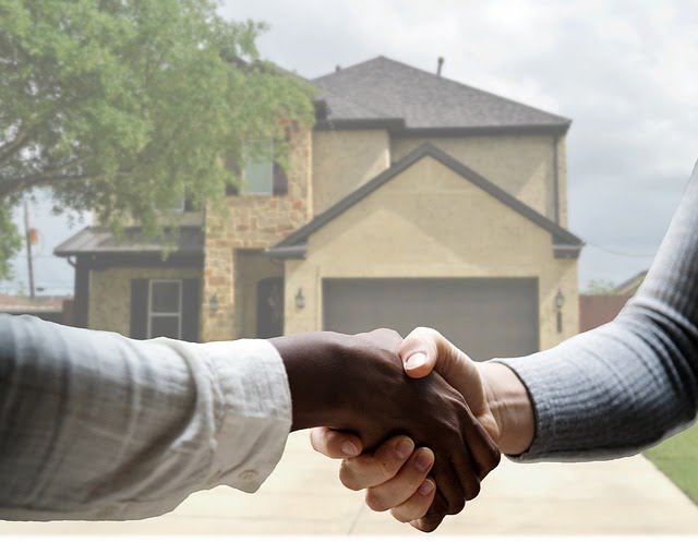 Two hands shaking in front of a two storey home in the background