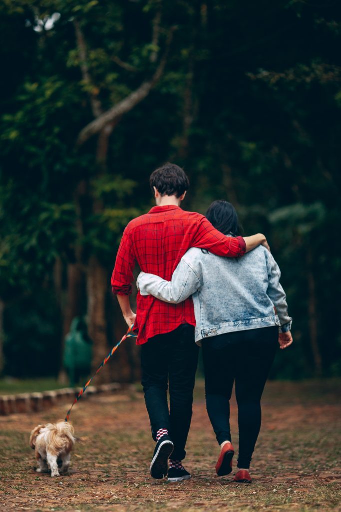 A young couple walking their dog away from the camera