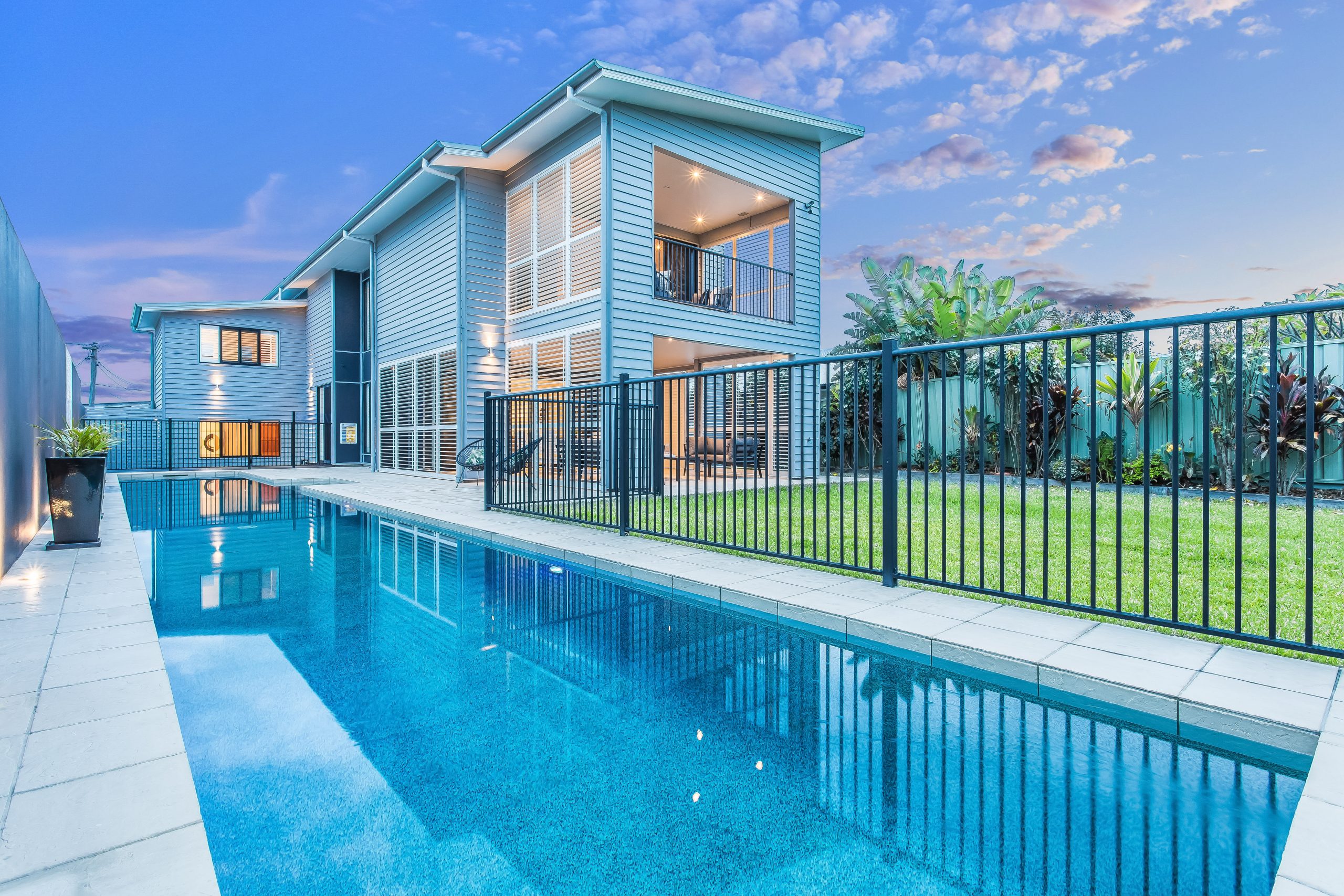 a large two storey blue house with fenced in swimming pool