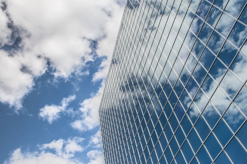 View of large glass building roof by clouds