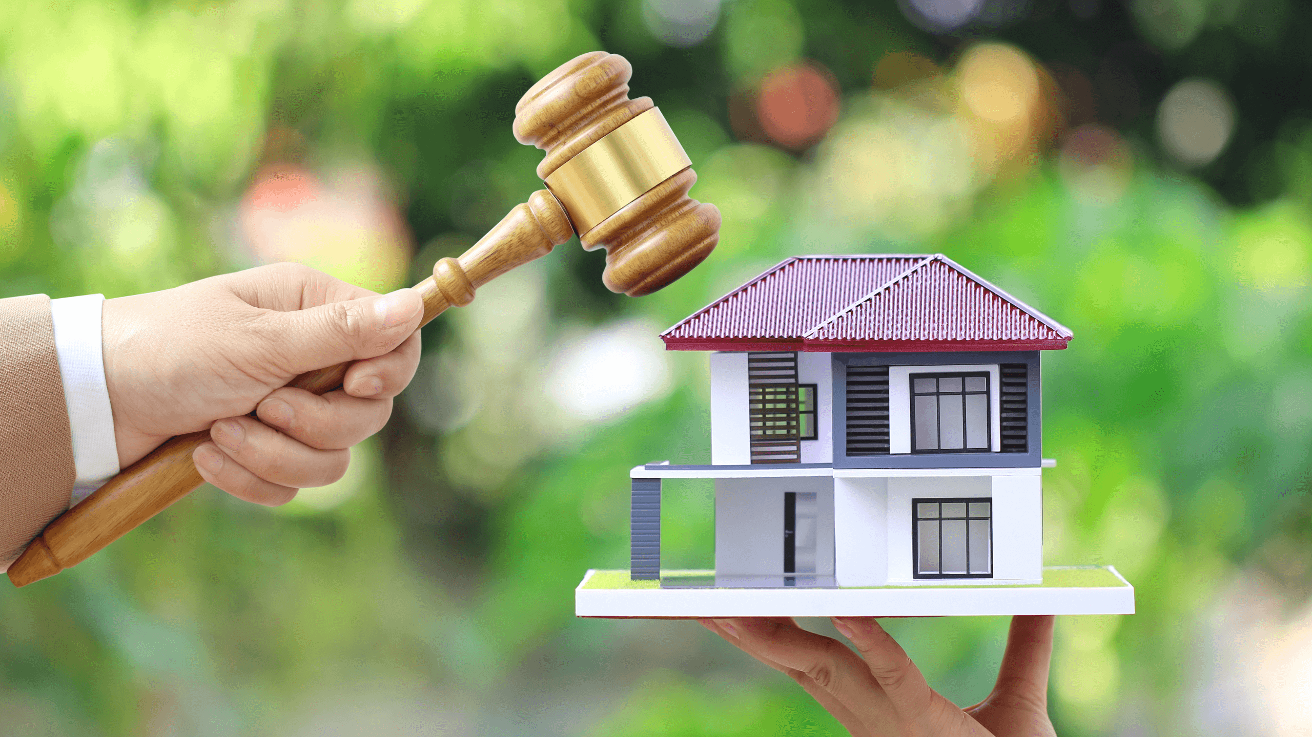 Hand holding a gavel above a model house, symbolising a property auction.